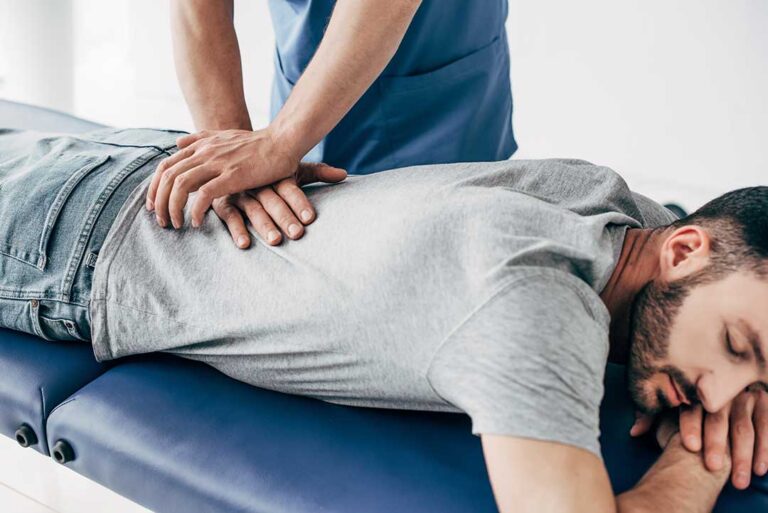A middle-aged person receives a gentle manual adjustment from a healthcare professional in a bright clinic room.